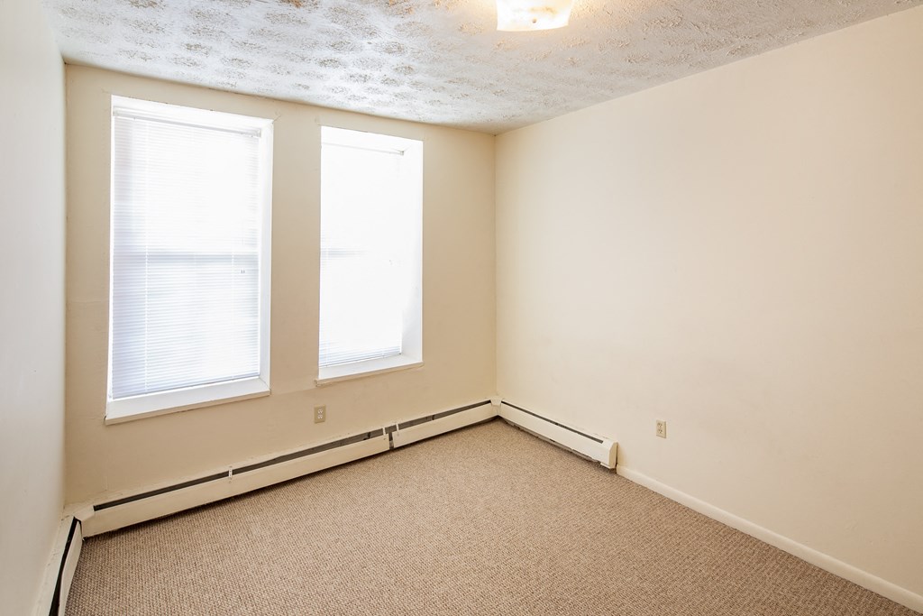 an empty room with two windows and a carpet