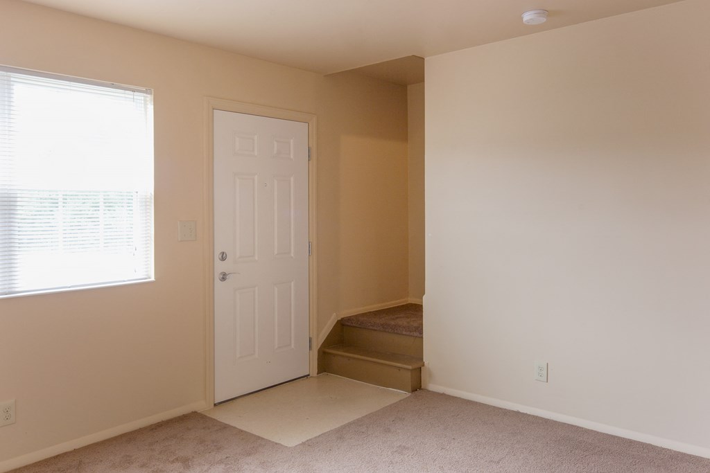 an empty room with stairs and a white door and a window