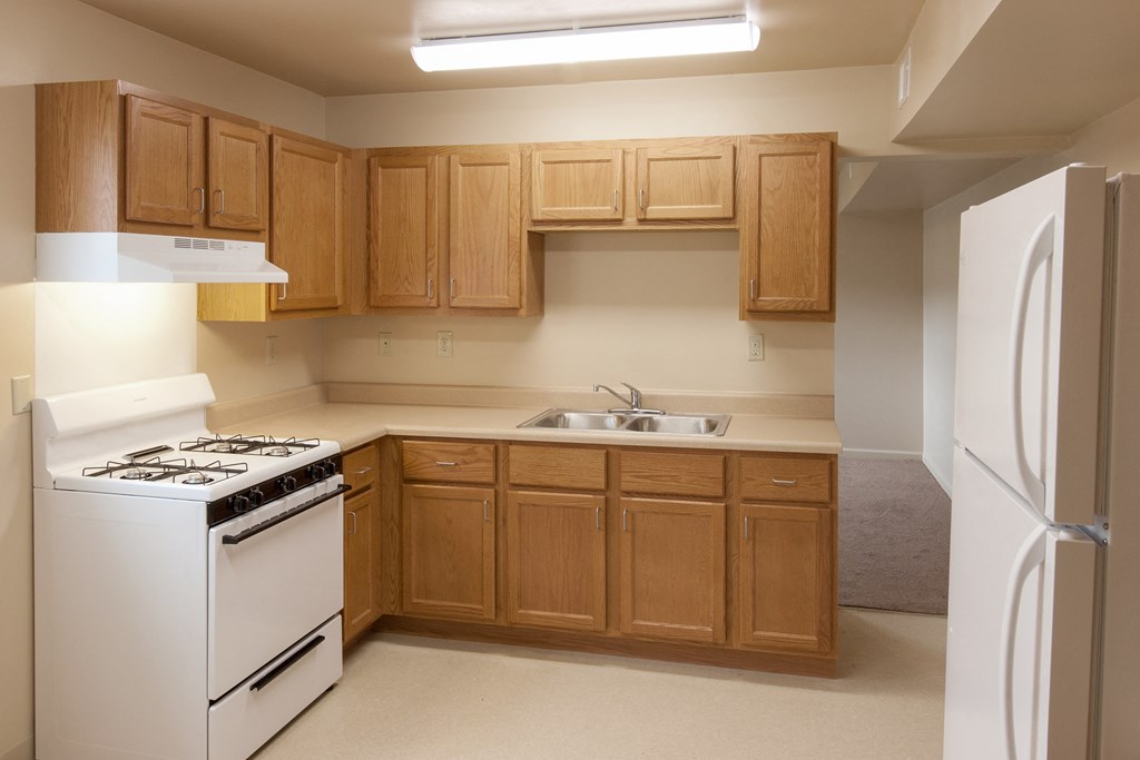 an empty kitchen with white appliances and wooden cabinets