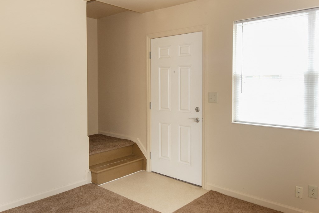 an empty room with stairs and a white door and a window