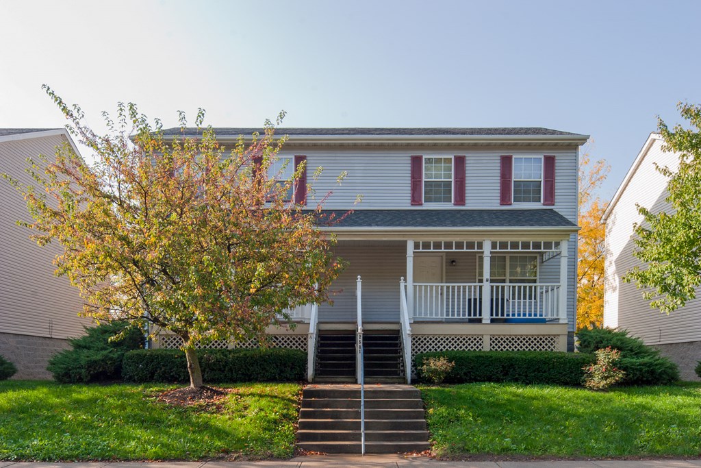 a white house with a porch and a tree in front of it