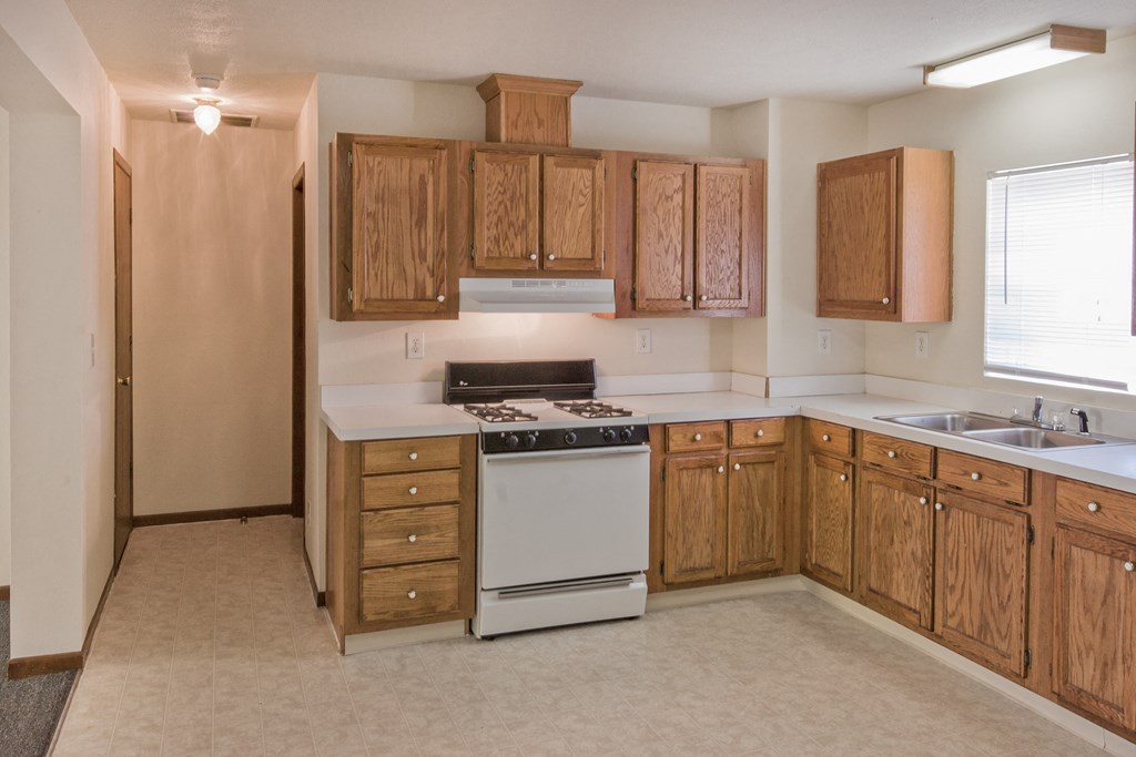 an empty kitchen with wooden cabinets and a white stove