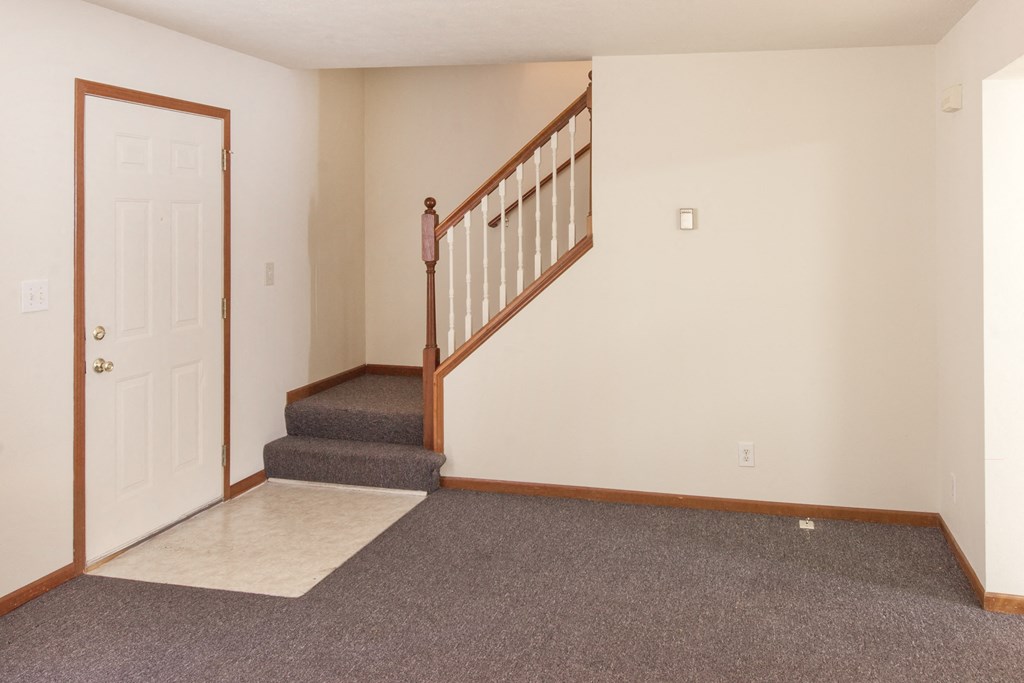 the entryway of a house with carpeted stairs and a door