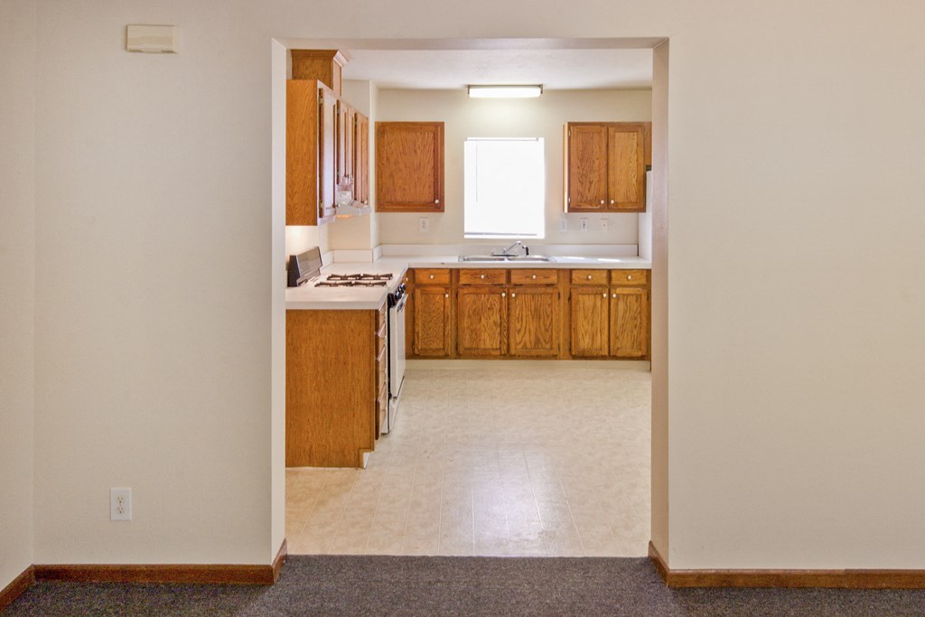 an empty kitchen with wooden cabinets and a white tile floor