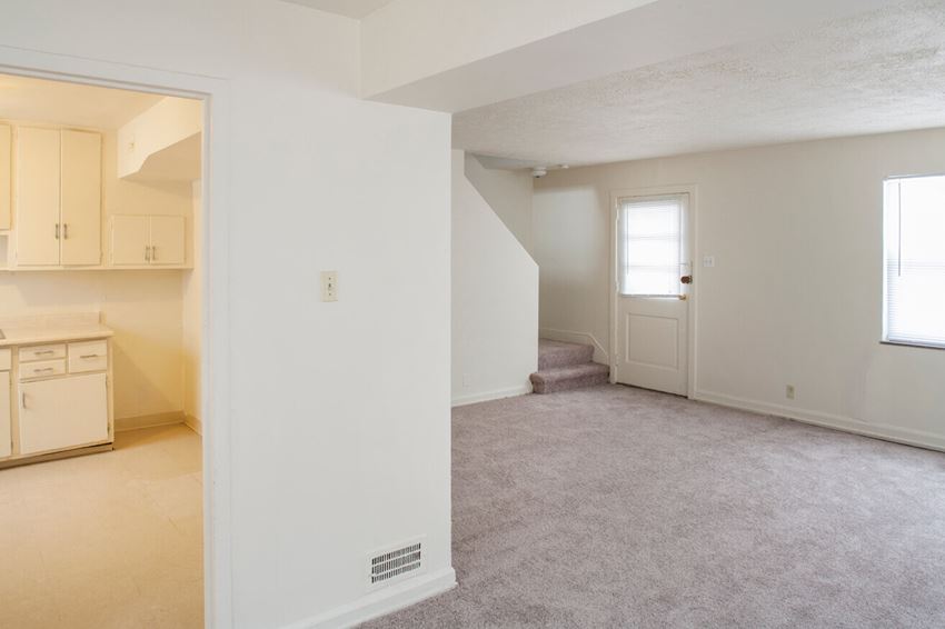 an empty living room and kitchen with a door to a staircase