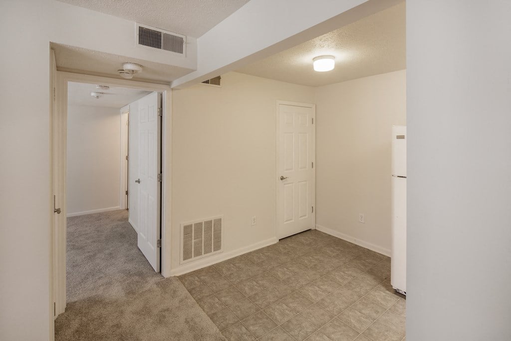 an empty living room with a door to a closet and a white refrigerator