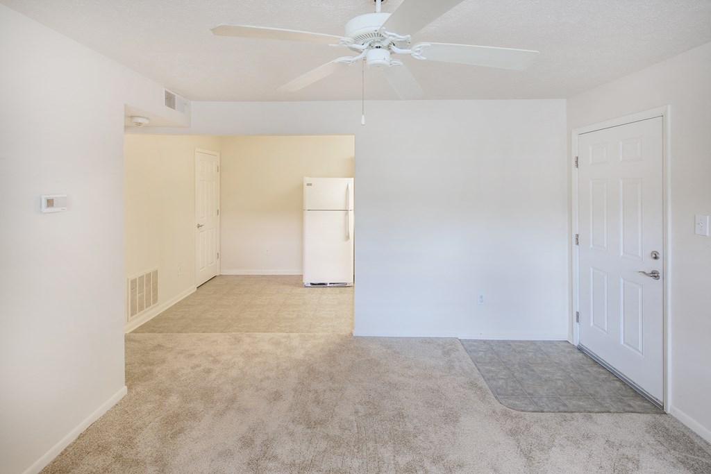 an empty living room with a ceiling fan and a white refrigerator