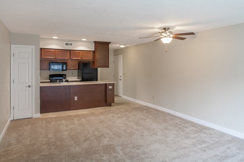 an empty living room with a kitchen and a ceiling fan