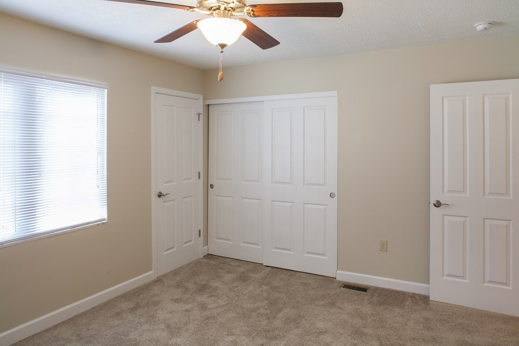 an empty bedroom with two doors and a ceiling fan