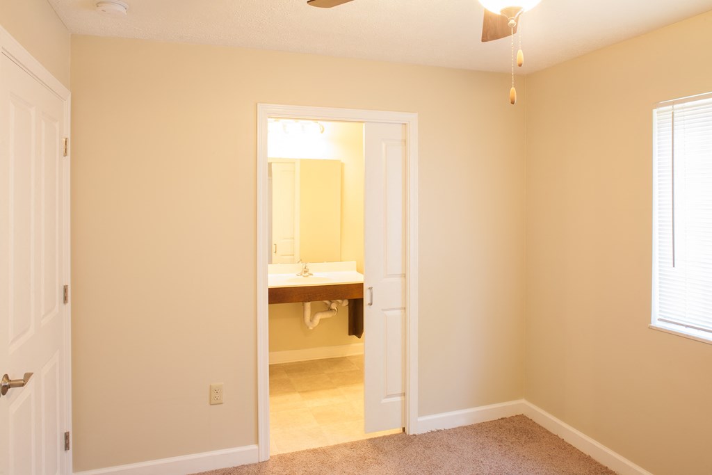a bedroom with a door to a bathroom with a sink and a mirror