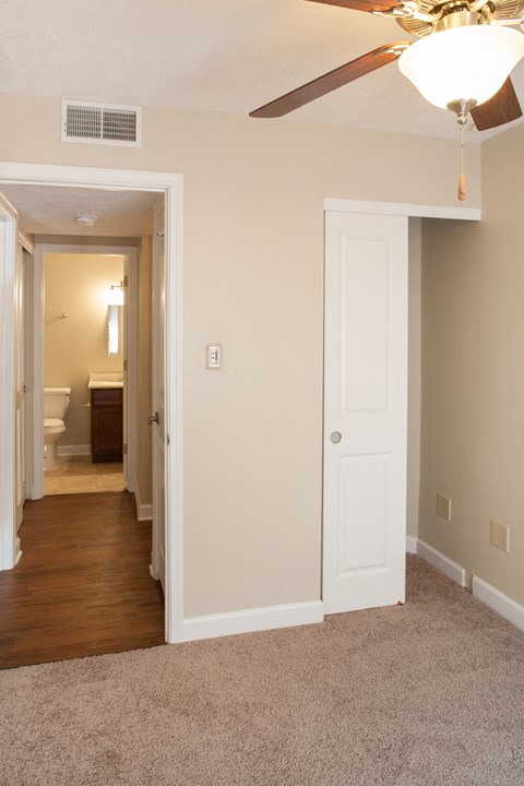 a bedroom with a ceiling fan and a hallway to a bathroom