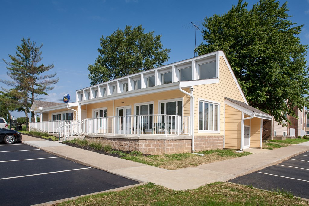 an exterior view of a yellow house with a porch and a parking lot