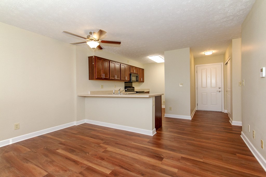 an empty living room with a kitchen and a ceiling fan