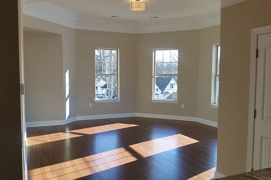 an empty living room with wooden floors and three windows
