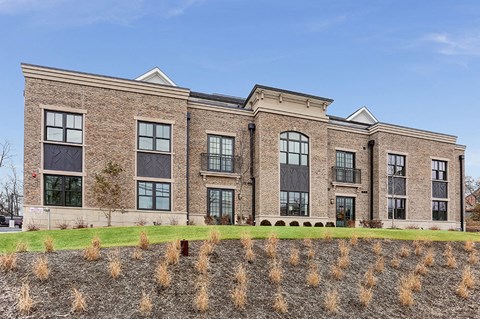 the front of a brick building with windows and a grass field