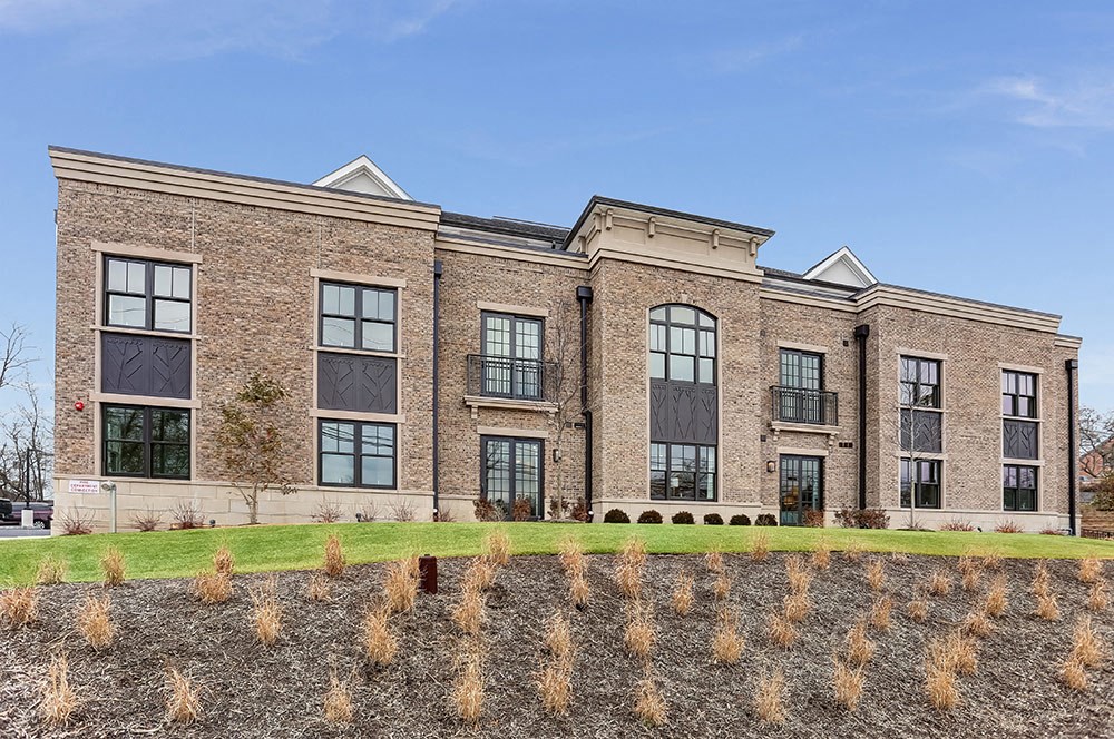 the front of a brick building with windows and a grass field