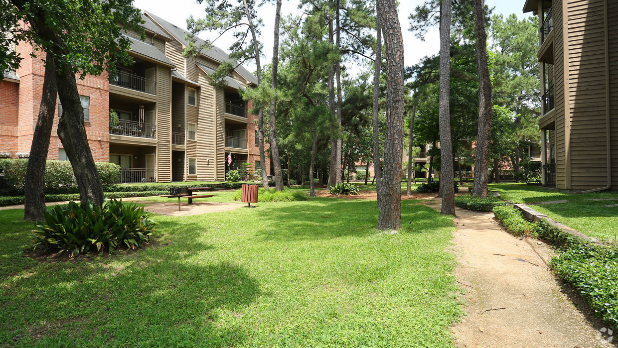 a grassy area with trees in front of apartment buildings