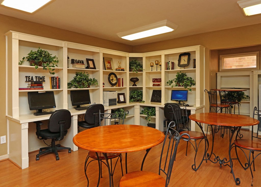 a computer room with tables and chairs and a bookshelf