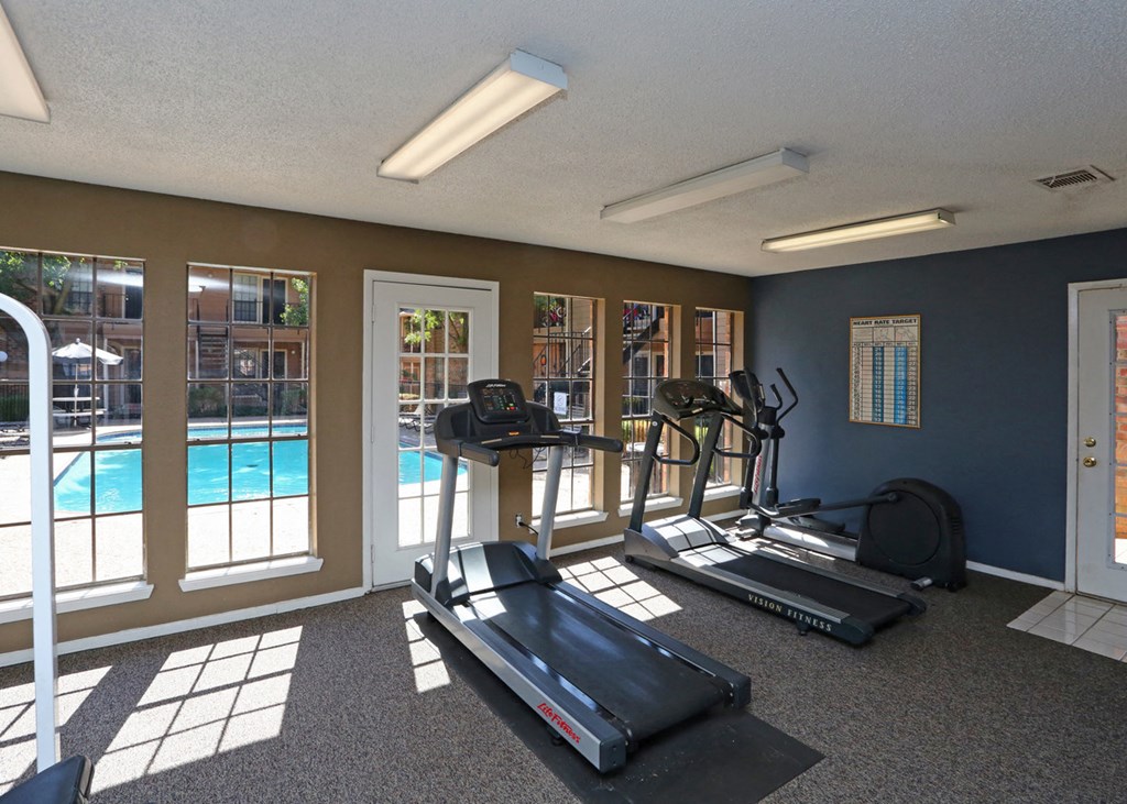 a gym with cardio equipment and a pool at the enclave at university crossings apartments