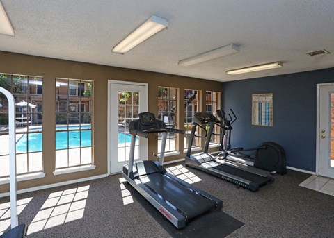 a gym with cardio equipment and a pool at the enclave at university crossings apartments