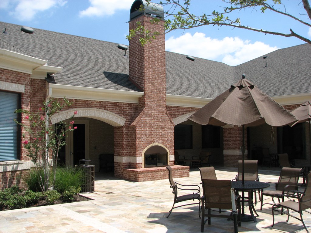 a patio with tables and umbrellas and a brick fireplace