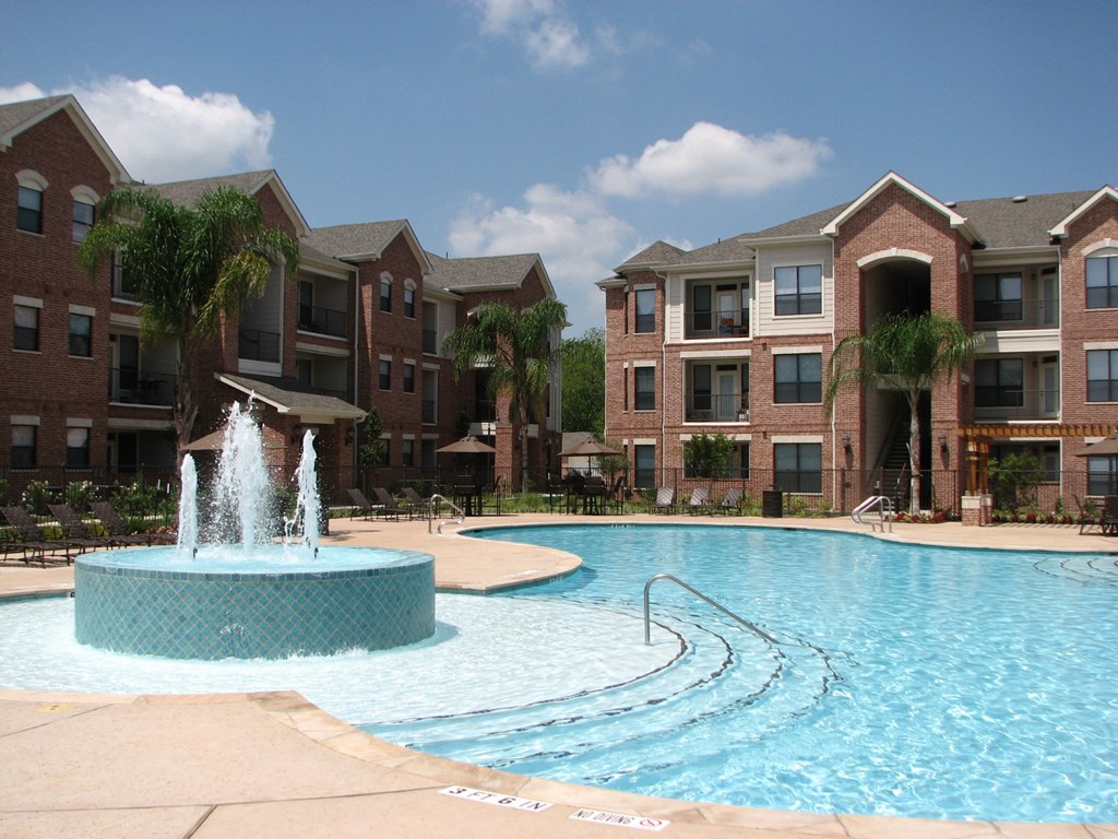 a large pool with a fountain in front of an apartment building