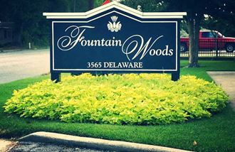 a sign for fountain woods with yellow flowers under it