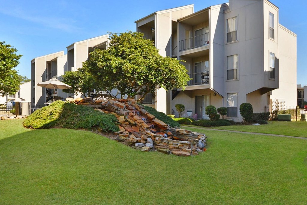 a rock formation in the grass in front of an apartment building