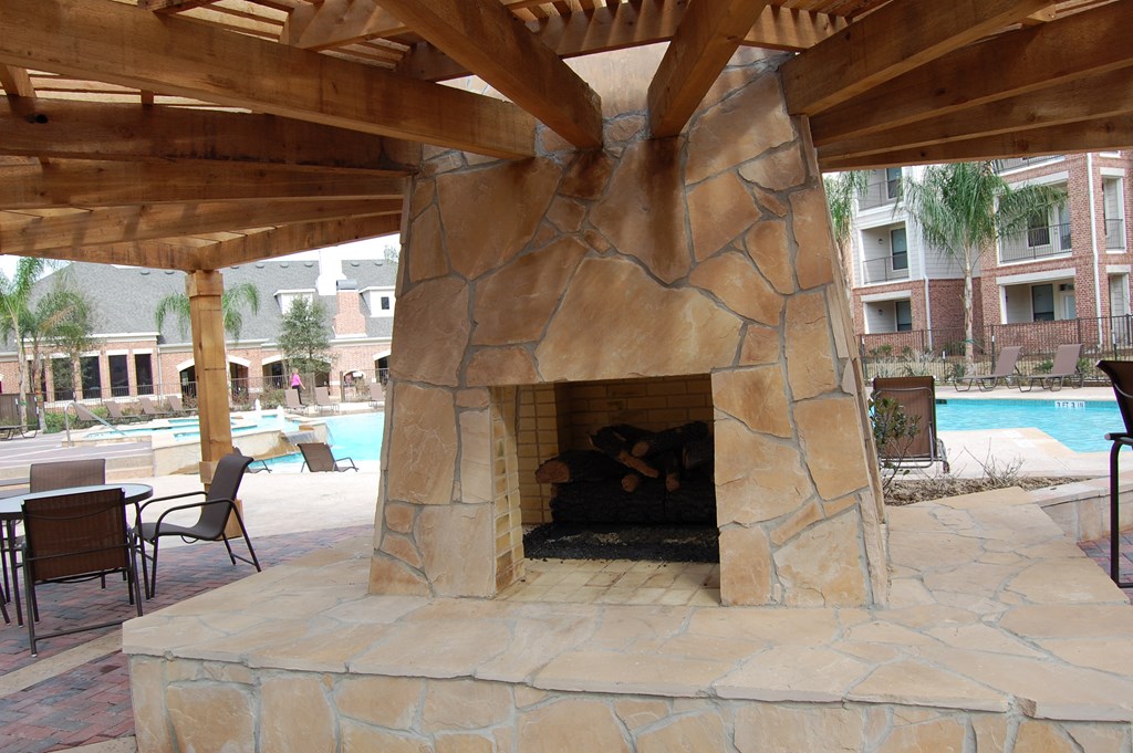 a large stone fireplace in a patio with a table and chairs