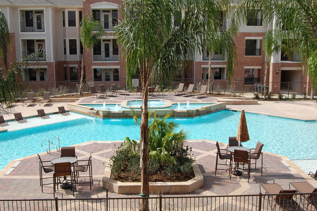 a swimming pool with chairs and trees in front of an apartment building