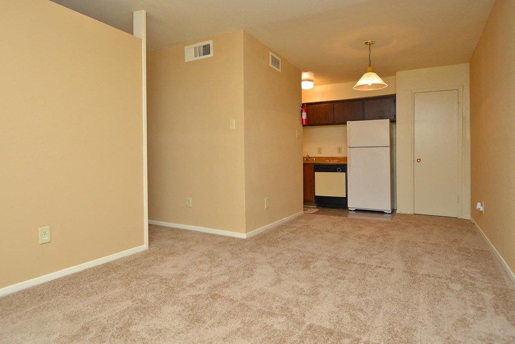 an empty living room and kitchen with a white refrigerator
