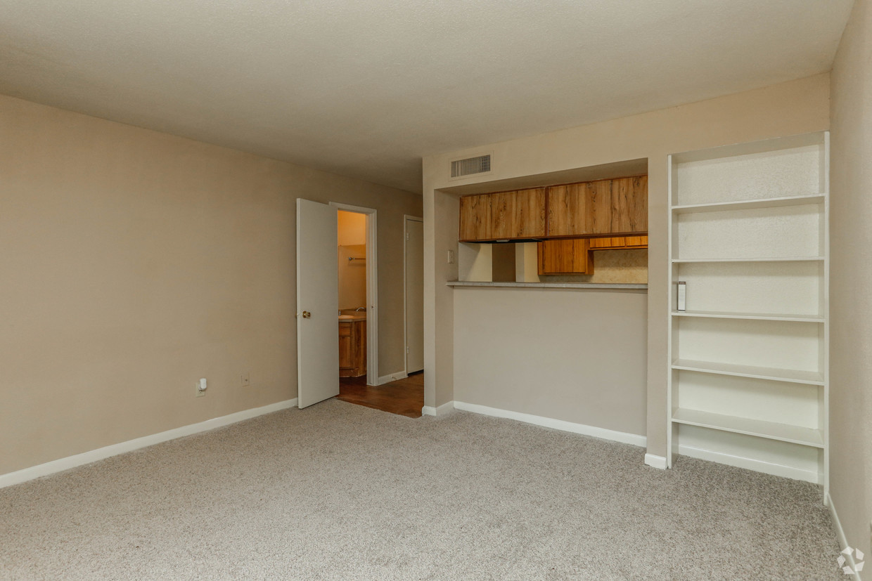 an empty living room with white shelves and a kitchen