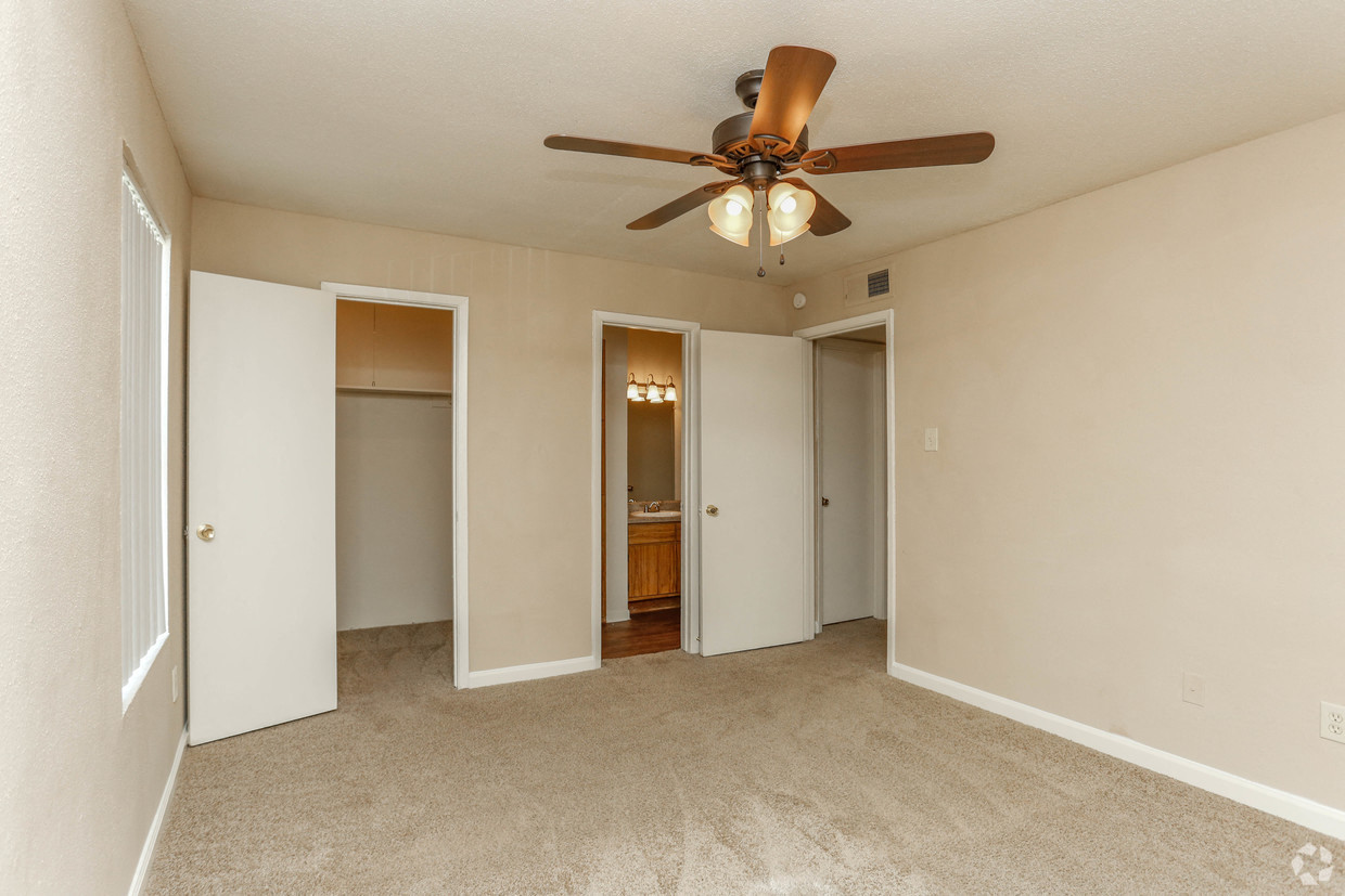 an empty living room with a ceiling fan and a door to a bathroom