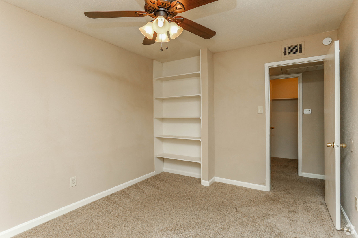 an empty bedroom with shelves and a ceiling fan