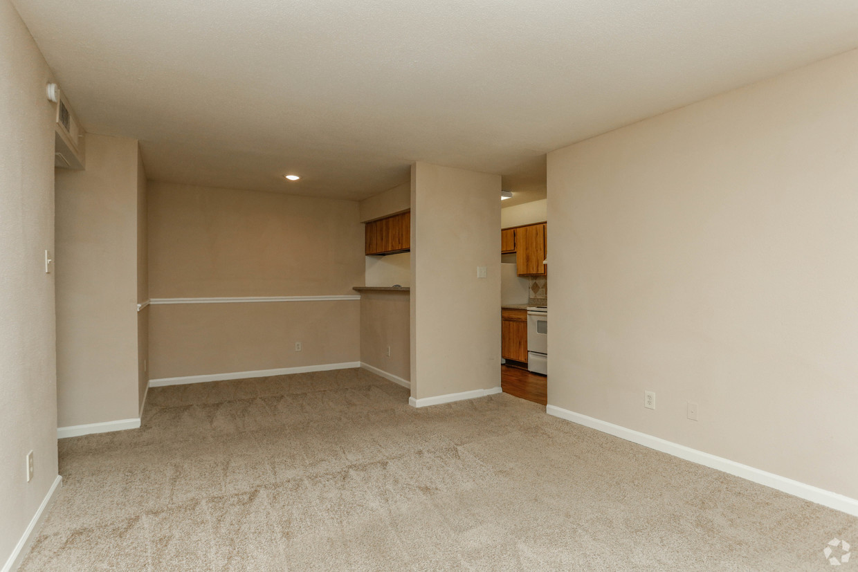 an empty living room with a kitchen in the background