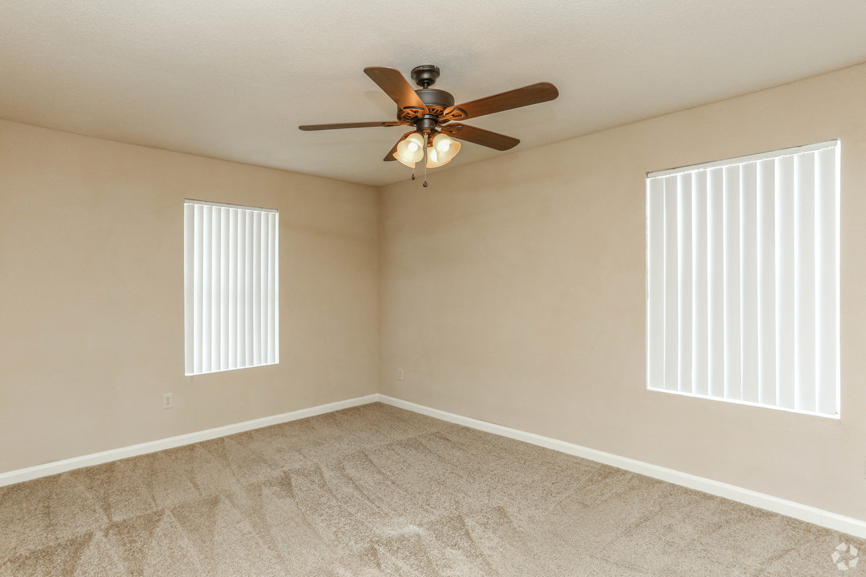 an empty living room with a ceiling fan and two windows