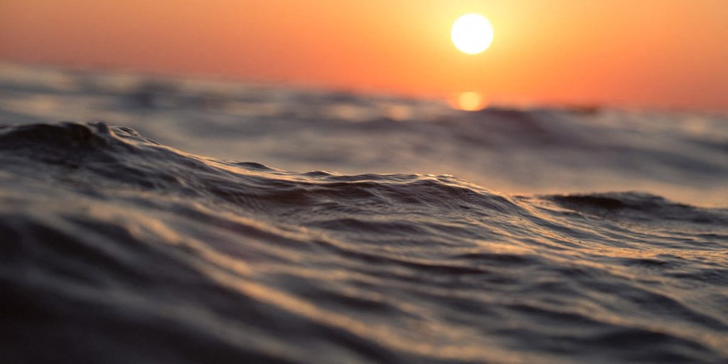 the sun setting over the ocean with waves in the foreground