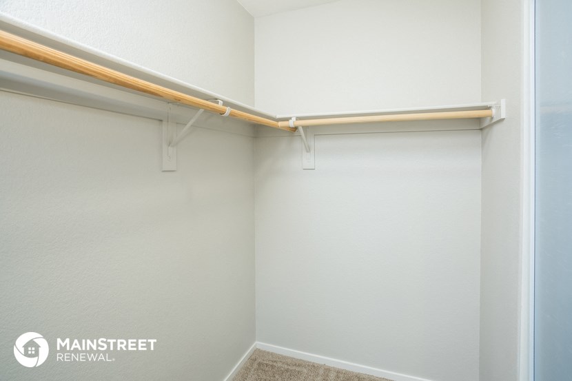 a walk in closet with a white wall and a pipe hanging from the ceiling