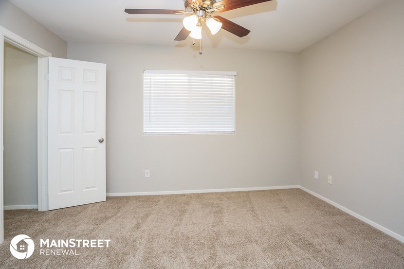 the bedroom of an apartment with carpet and a ceiling fan