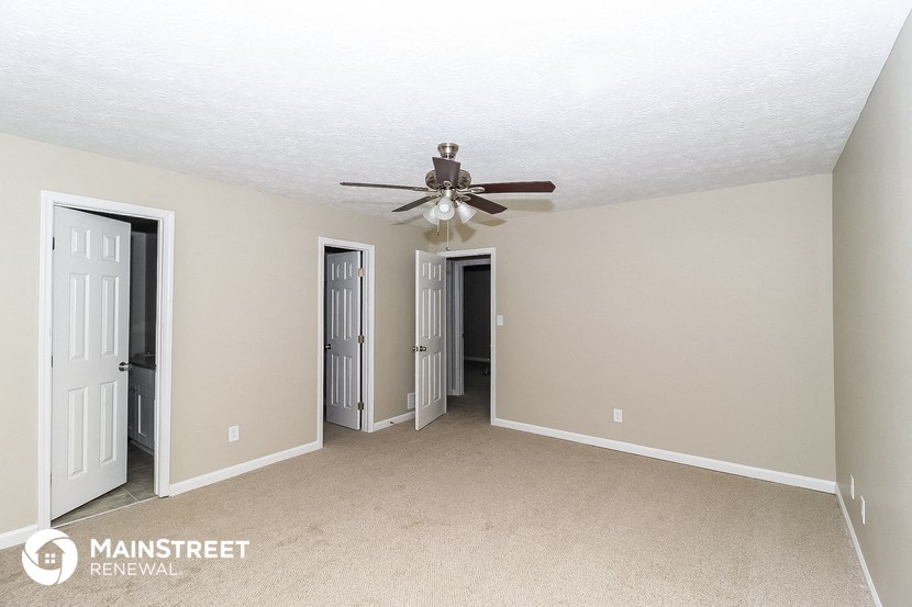 a bedroom with a ceiling fan and doorways to two closets