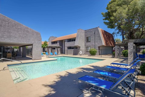 A pool with sun loungers and a building in the background.