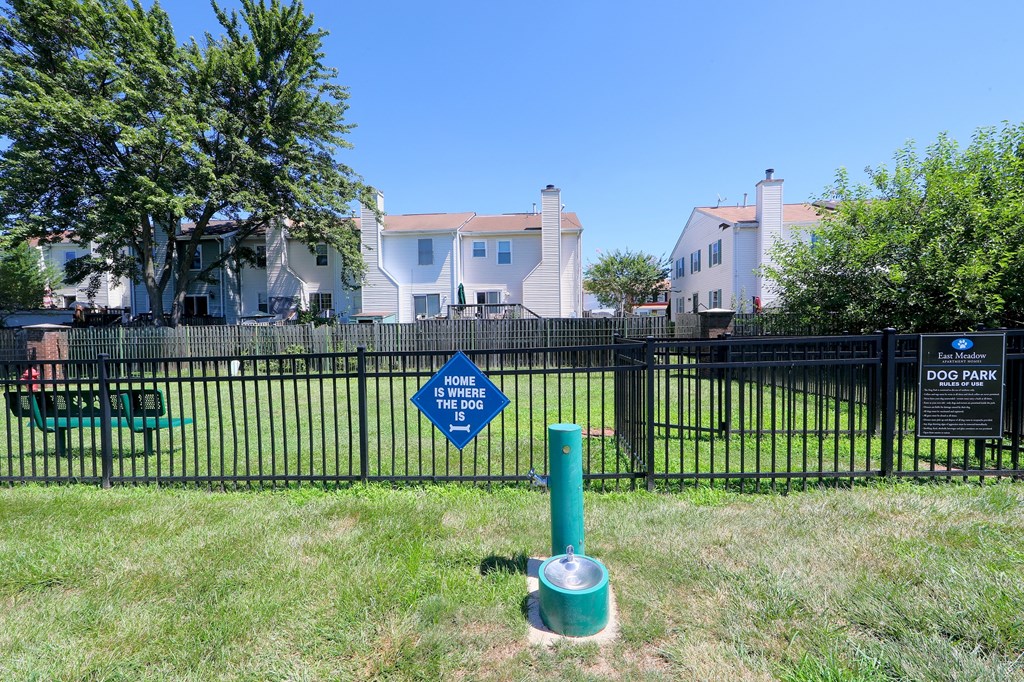 a green fire hydrant in front of a fence with houses behind it