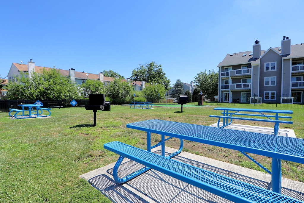 a blue picnic table and benches in a park with apartments in the background