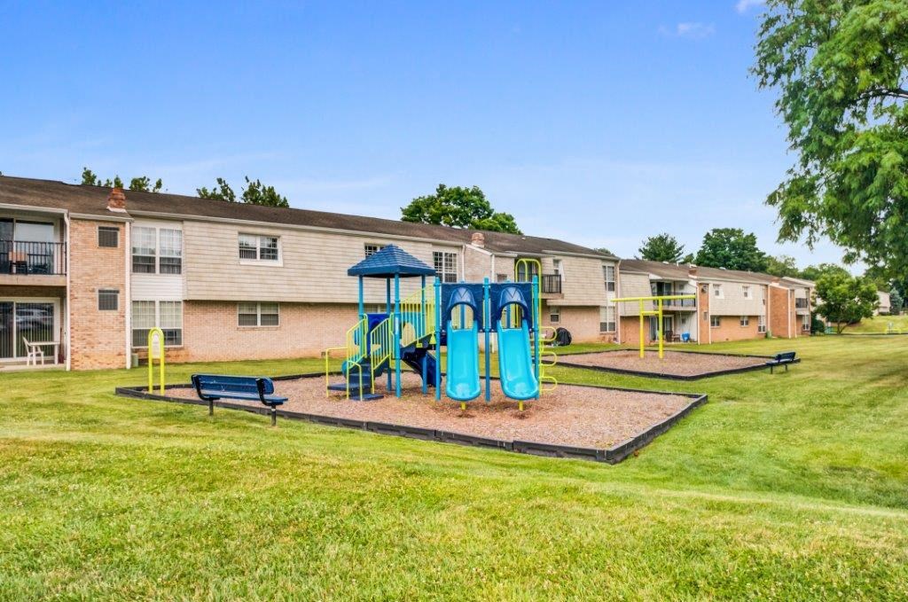 a playground with a blue playset in front of an apartment building