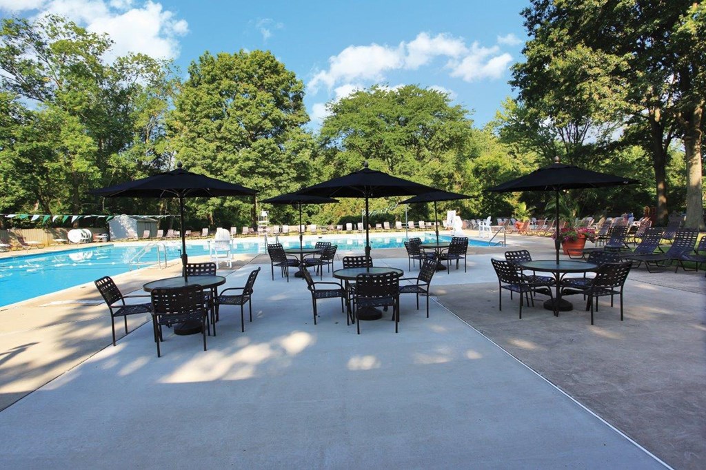 a patio with tables and umbrellas next to a swimming pool