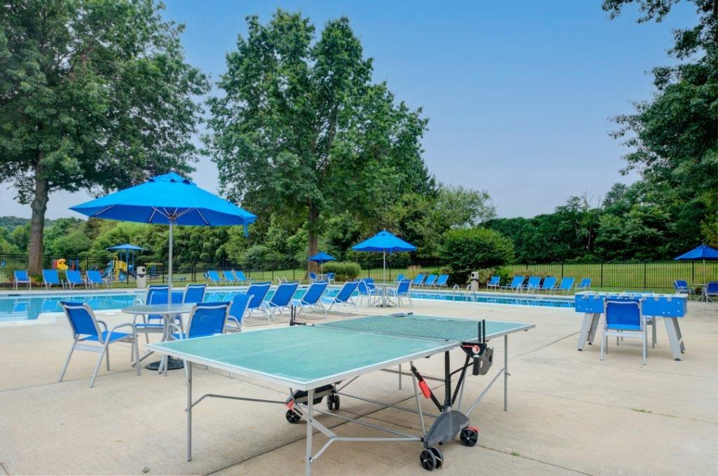 a ping pong table with chairs and umbrellas near a pool