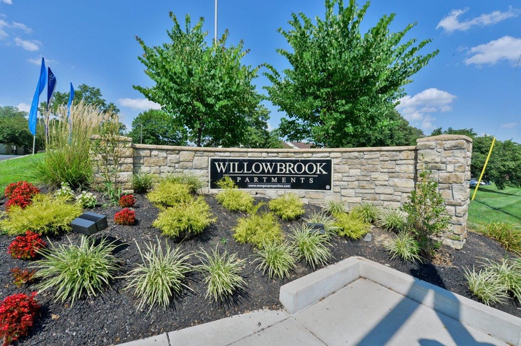 the sign for willowbrook apartments in front of a stone retaining wall with plants