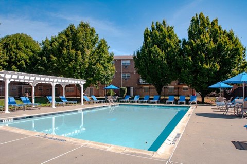 a swimming pool with chairs and umbrellas and a building in the background
