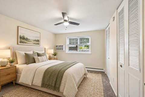 A bedroom with a bed, a ceiling fan, and a window with a view of a fence and trees.