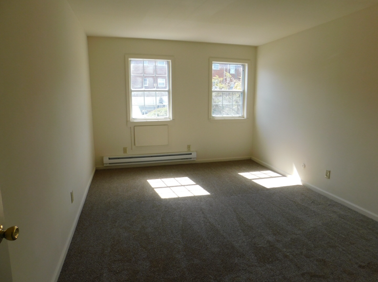 an empty living room with two windows and carpeting